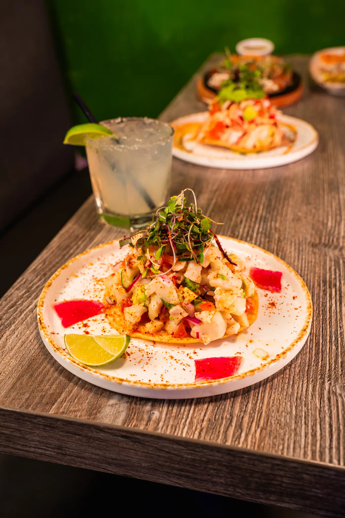 Shrimp ceviche tostada with microgreens and lime, margarita behind