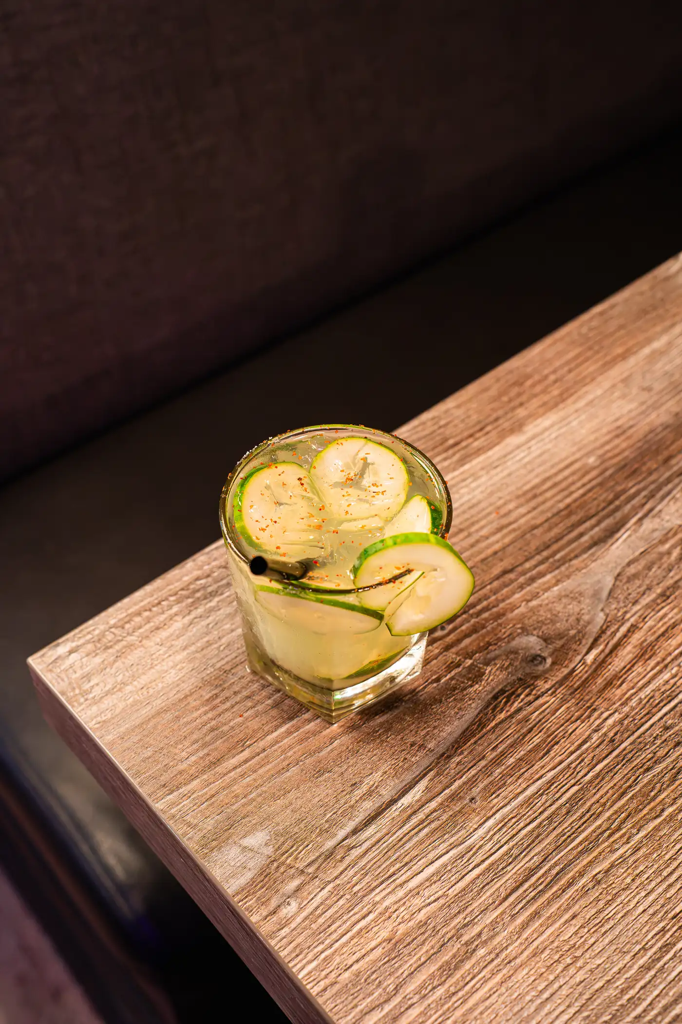 Cucumber-ribbon margarita on a wood table edge with a moody backdrop