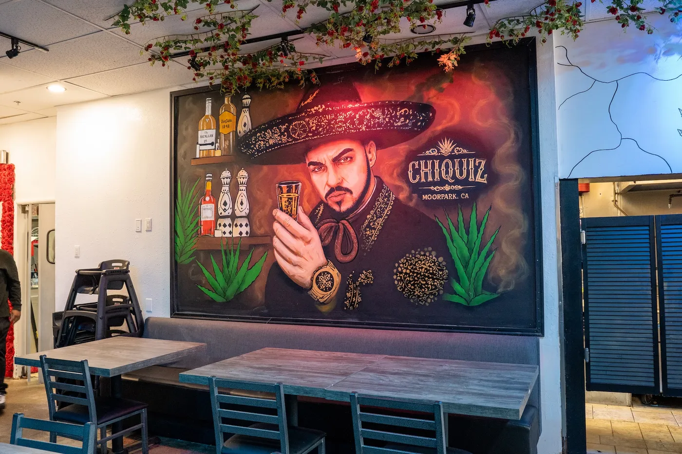 Charro Chiquiz mural with sombrero figure, tequila bottles and agave behind the communal table
