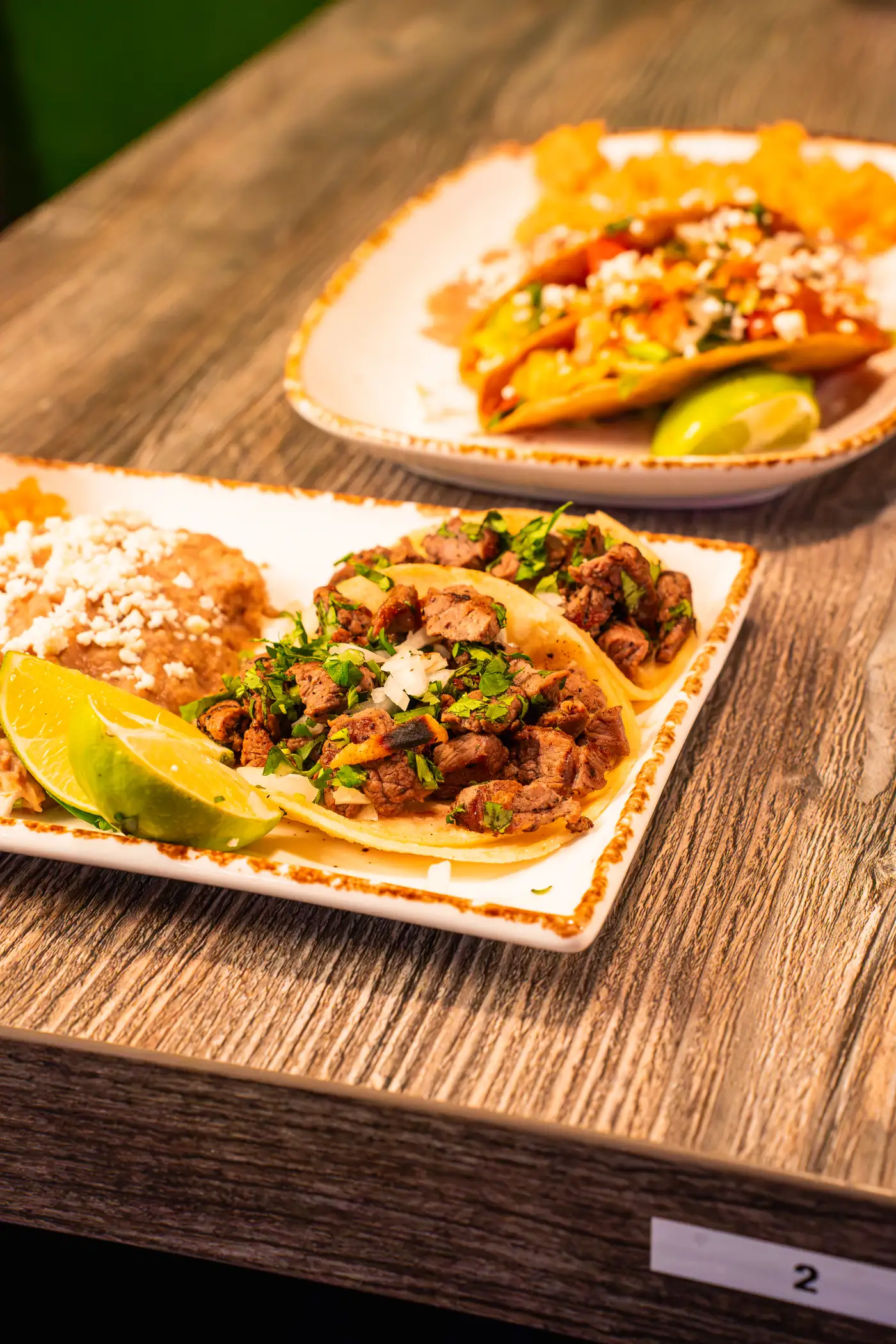 Carne asada tacos with cotija, lime and beans, second plate behind